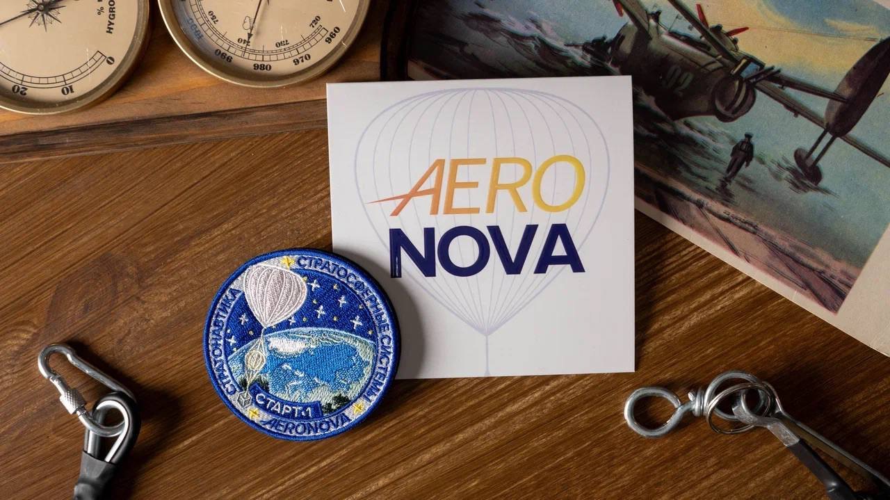 AERONOVA brand card, an embroidered stratospheric-systems mission patch, brass aviation instruments and a vintage airship illustration laid on a wooden desk.