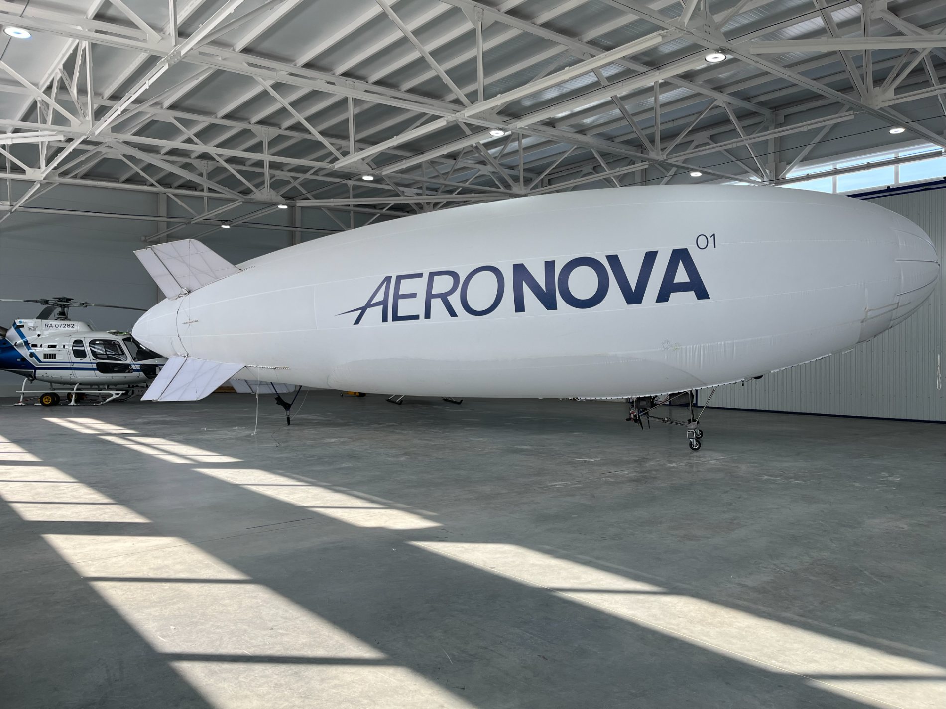 NOVA-01 airship in a sunlit hangar, full side profile, AERONOVA livery along the hull.